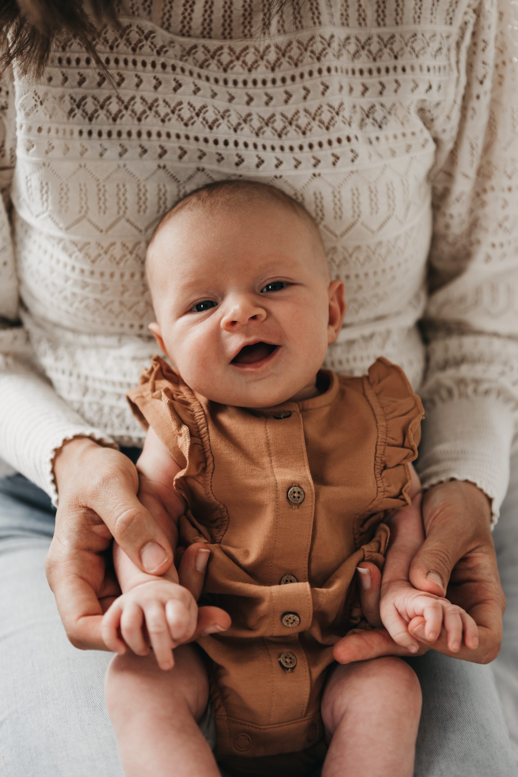Smiling baby in a brown outfit on her mother’s lap