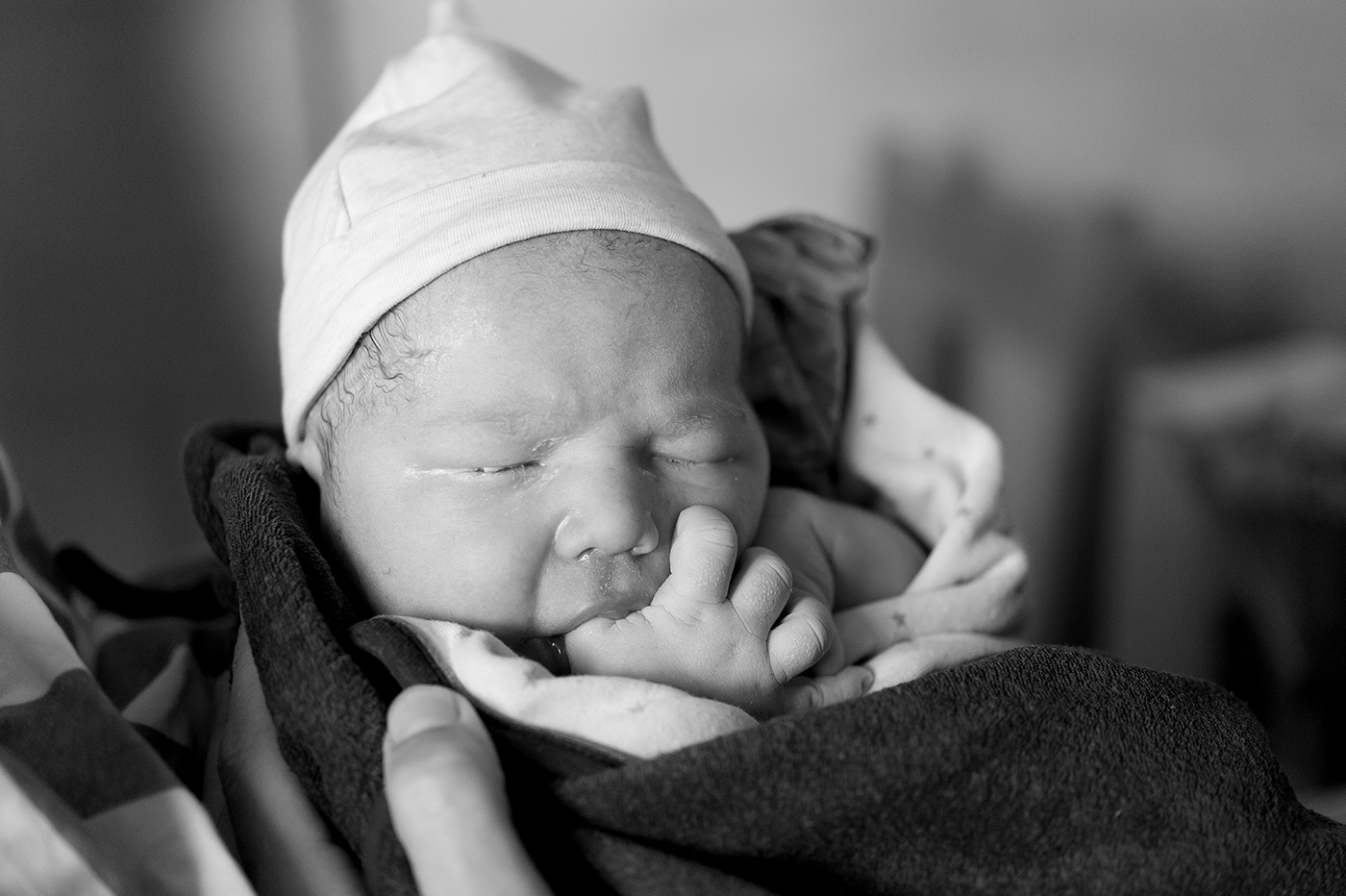 Zwart-witfoto van een pasgeboren baby met een mutsje, in een deken gewikkeld