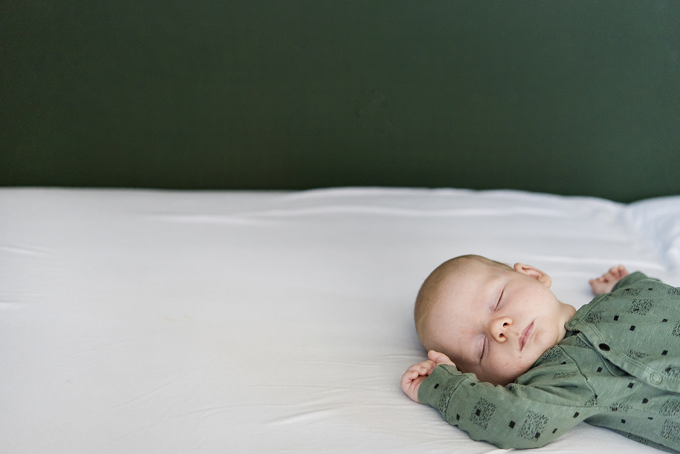 Baby in een groen pakje slaapt op een wit bed