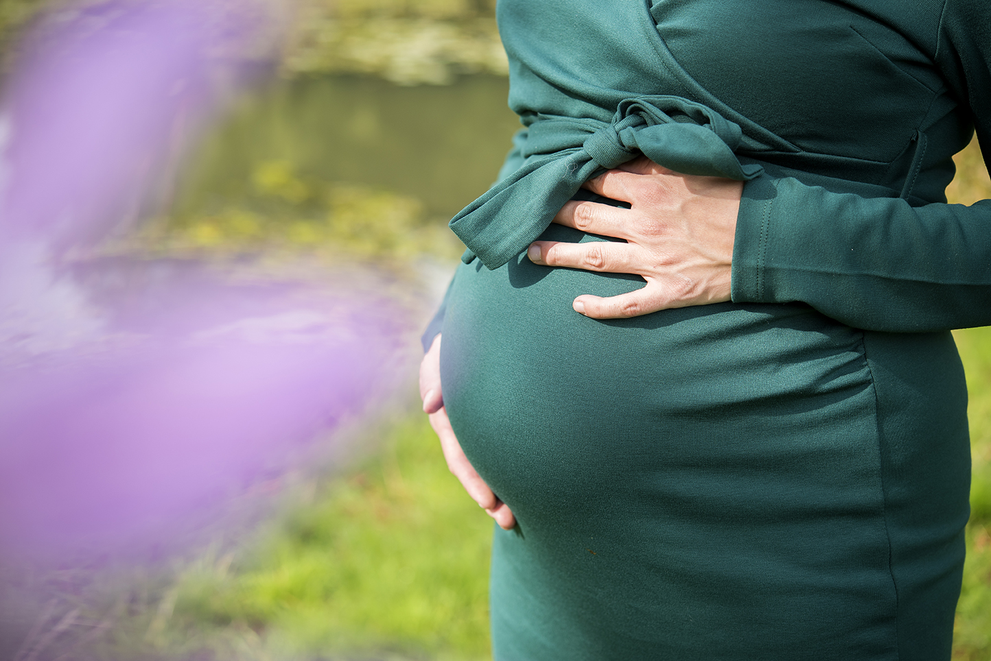 Zwangere vrouw in een groene jurk houdt haar buik vast